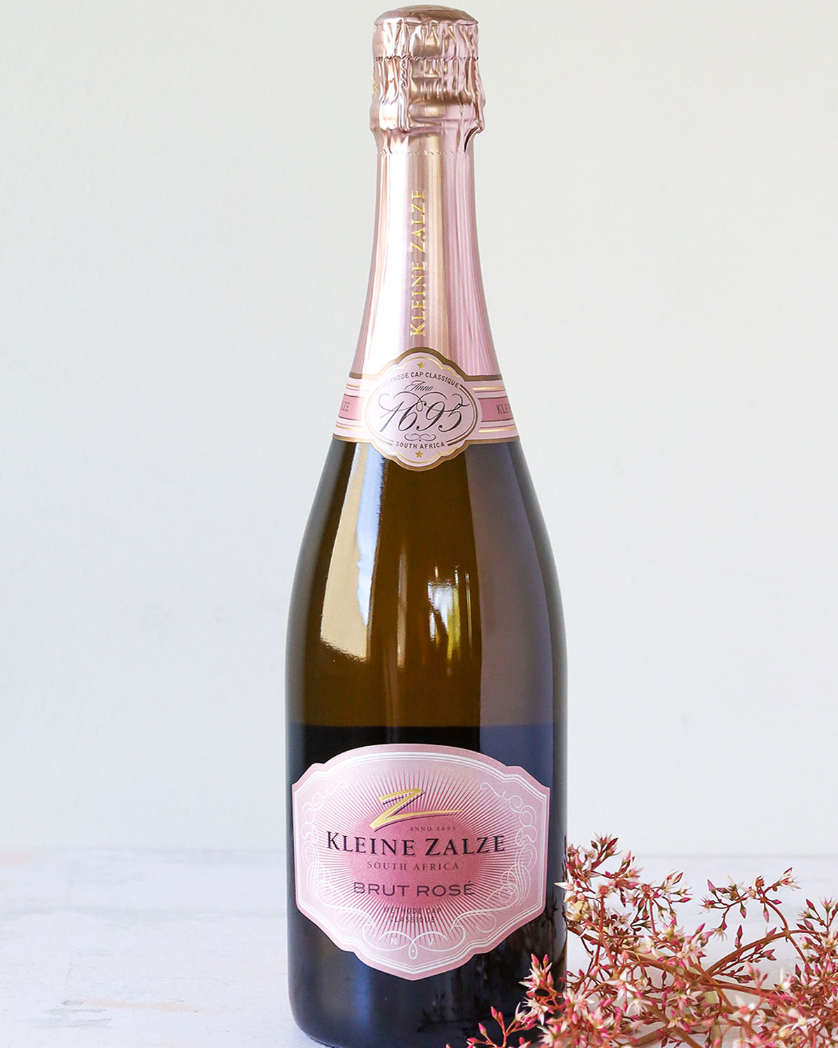 Eine Flasche Kleine Zalze Brut Rosé Sekt aus Südafrika mit einem mit rosa Folie umwickelten Hals und einem dekorativen rosa-weißen Etikett auf einer dunklen Glasflasche.