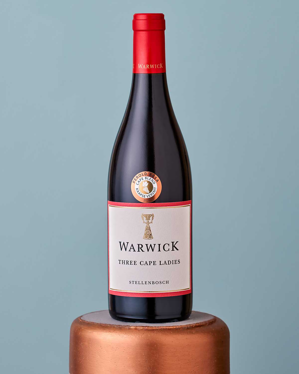 Eine Flasche Warwick Three Cape Ladies Rotwein aus Stellenbosch mit einem rot-weißen Etikett mit goldenen Akzenten und einer roten Folienkapsel über dem Korken.