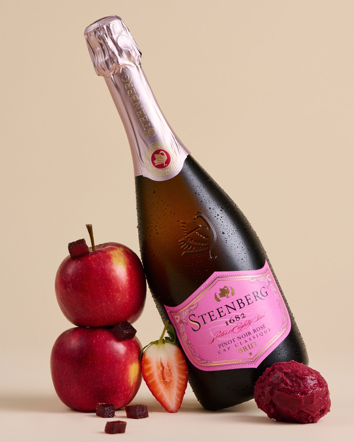 Eine Flasche Steenberg 1682 Pinot Noir Rosé Sekt mit rosafarbenem Folienverschluss und rosafarbenem Etikett mit goldenen Akzenten und schwarzem Text auf der Vorderseite.