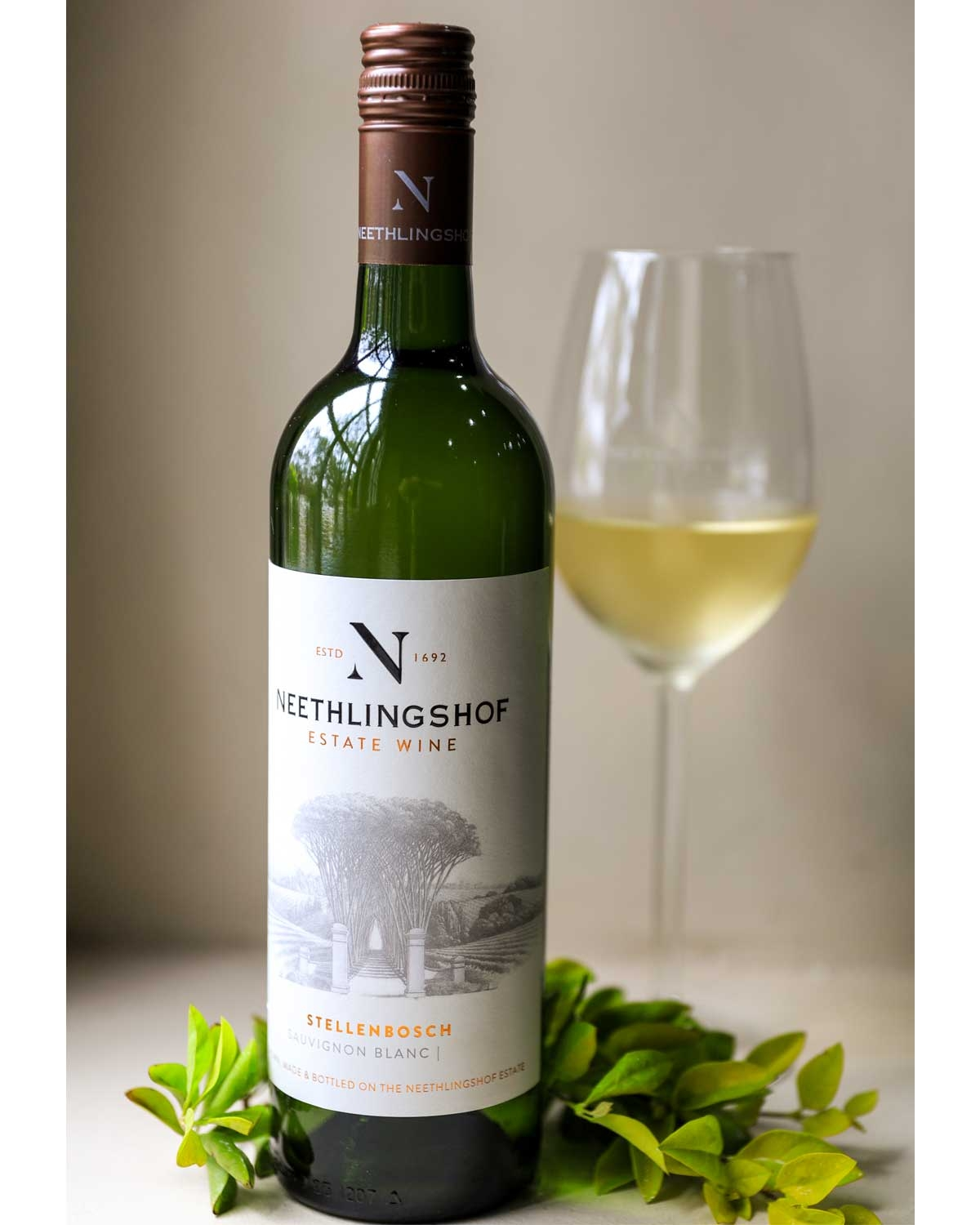 Eine grüne Flasche Neethlingshof Estate Wine Sauvignon Blanc aus Stellenbosch mit einem cremefarbenen Etikett mit einer Abbildung des Weinbergs und einem kupferfarbenen Schraubverschluss.
