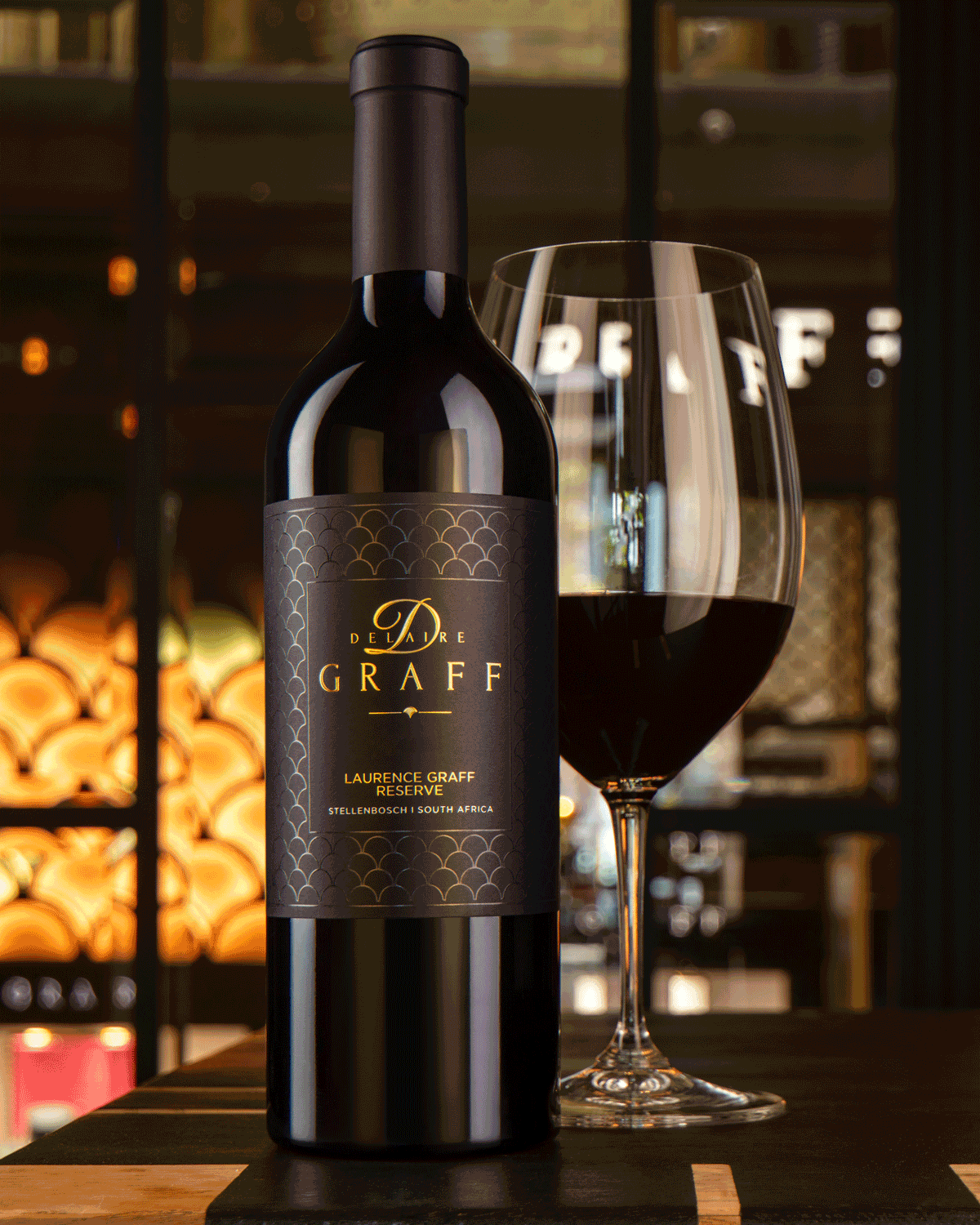 Eine Flasche Delaire-Graff-Rotwein steht neben einem gefüllten Weinglas auf einem Tisch, mit schwach beleuchteten Weinregalen und verschwommenen Regalen im Hintergrund.