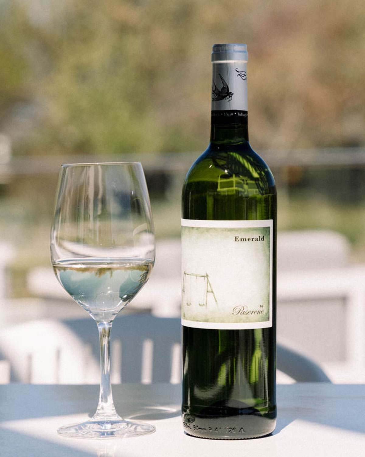 Eine grüne Glasweinflasche mit der Aufschrift Emerald von Pasarene zeigt die Illustration einer leeren Schaukel vor einem hellen, nebligen Hintergrund.