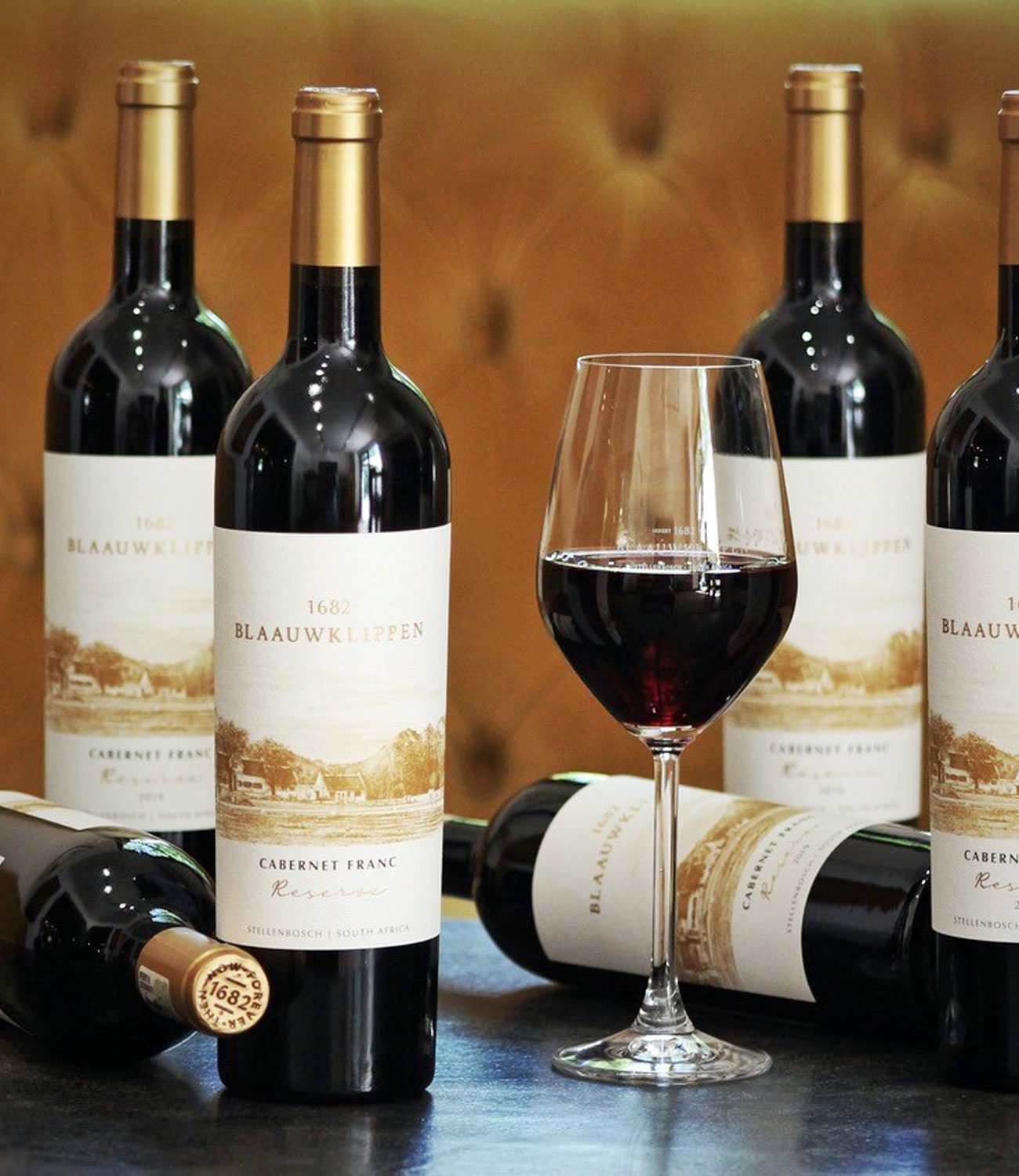 Eine Flasche Blaauwklippen 1682 Cabernet Franc Reserve Wein mit einem Goldfolienverschluss und einem cremefarbenen Etikett mit einer Illustration eines Weinbergs und von Gebäuden, aus Stellenbosch, Südafrika.