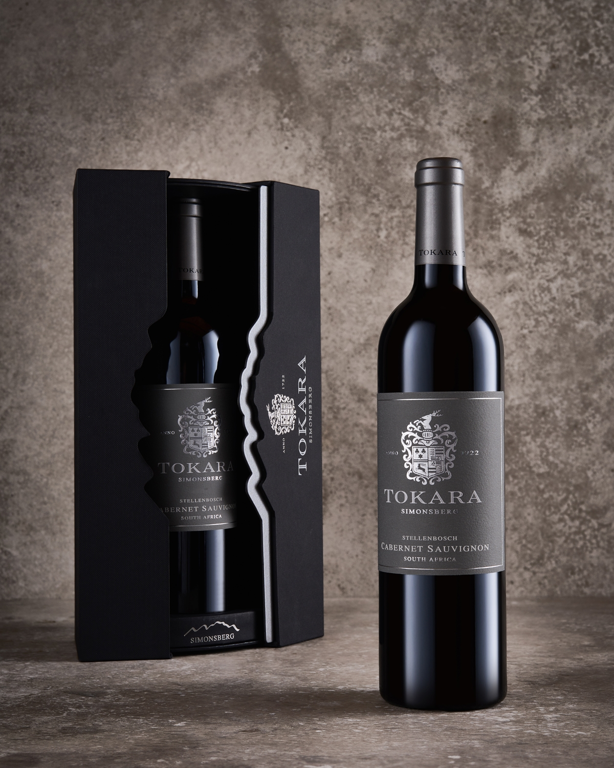 Eine Flasche Tokara Cabernet Sauvignon steht neben dem passenden schwarzen Geschenkkarton. Beide sind mit silbernen Etiketten und einem eleganten Branding versehen und stehen vor einem strukturierten, neutralen Hintergrund.