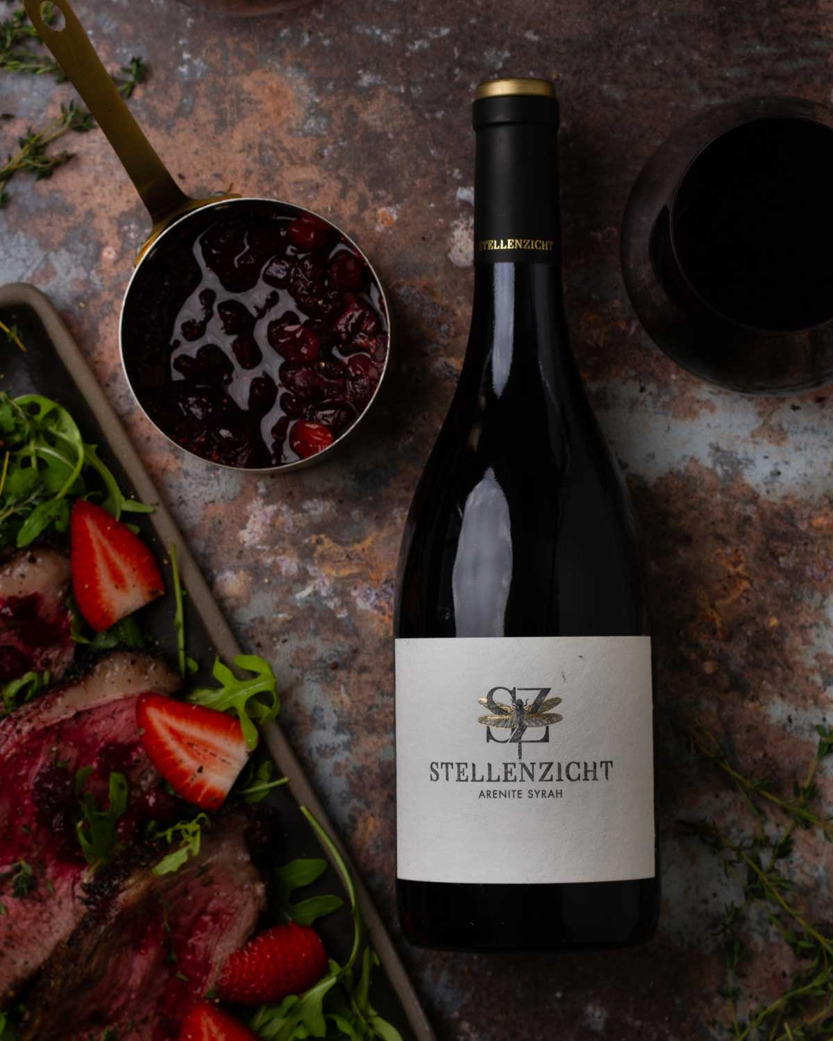 Eine dunkle Weinflasche mit einem hellbeigen Etikett mit der Aufschrift Stellenzicht Arenite Syrah und einem goldgeprägten Emblem über dem Namen. Hals und Deckel der Flasche sind mit einer schwarzen Folie überzogen.