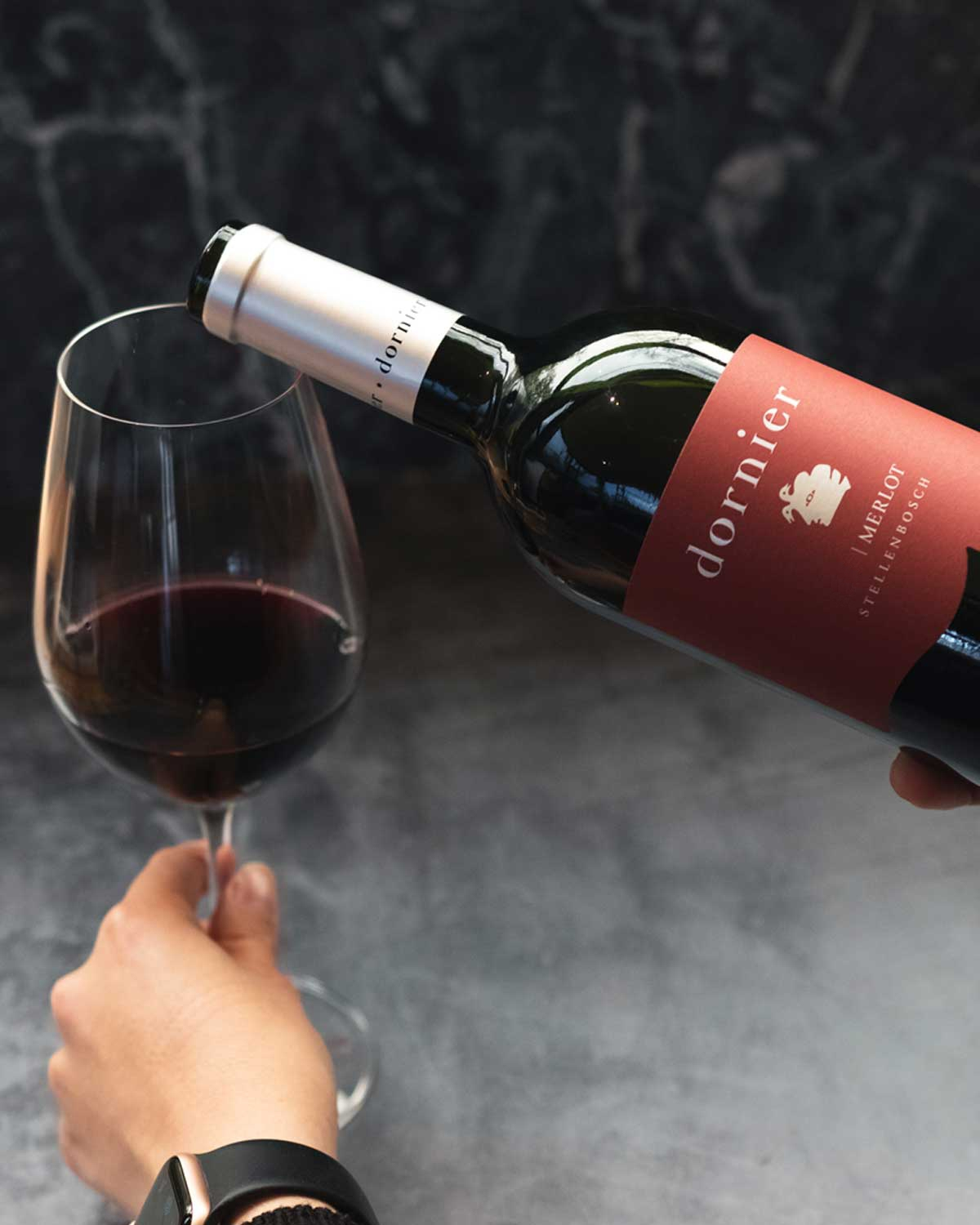 Eine Flasche Dornier Merlot-Wein aus Stellenbosch mit kastanienbraunem Etikett, silbernem Verschluss und weißem Text, der den Markennamen und die Weinangaben enthält.