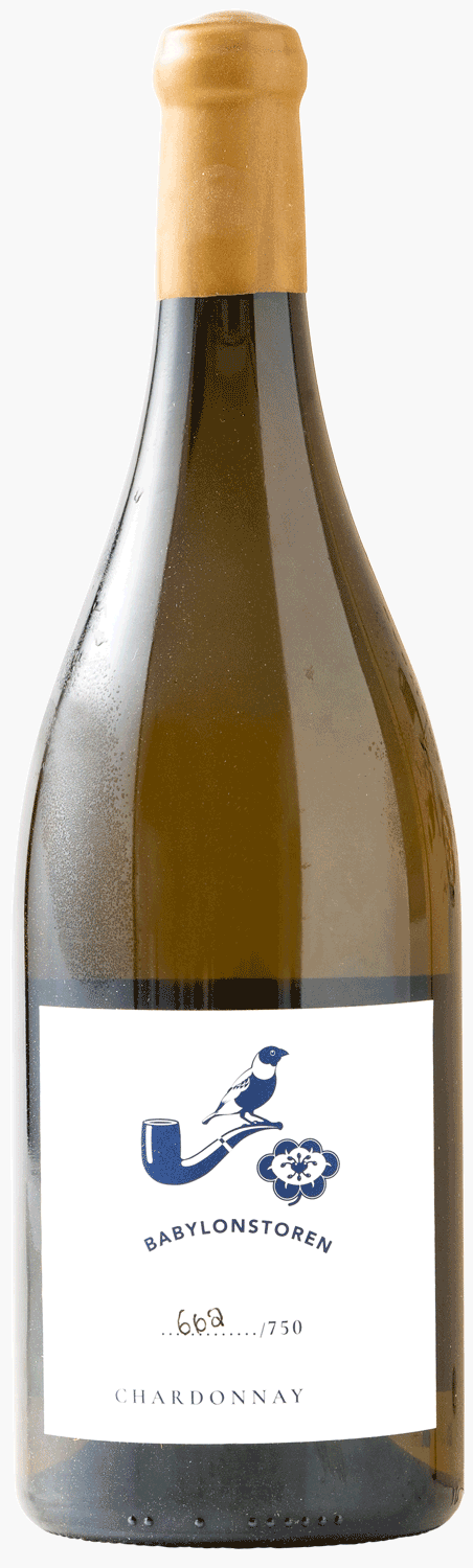 Eine Flasche Babylonstoren Chardonnay-Wein mit weißem Etikett steht vor einer aufrecht stehenden Holzkiste mit eingraviertem Babylonstoren-Logo und floralem Muster.
