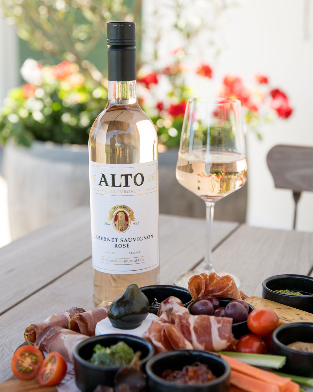 Eine Flasche Alto Stellenbosch Cabernet Sauvignon Rosé mit einem weiß-goldenen Etikett, auf dem das Wappen des Weinguts und der Text "Stellenbosch, Südafrika" zu lesen sind.