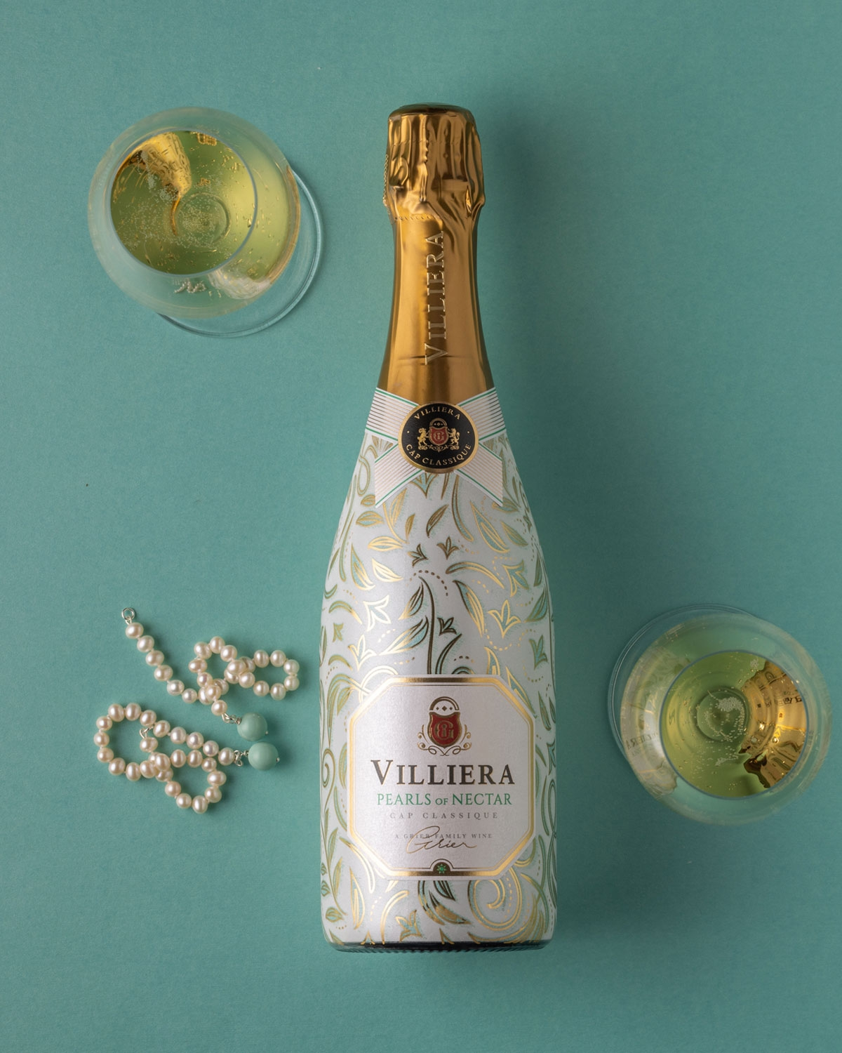 Eine Flasche Villiera Pearls of Nectar Sekt mit Goldfolienverschluss, weiß-goldenem Schmucketikett und elegantem Blattmuster auf der Flasche.
